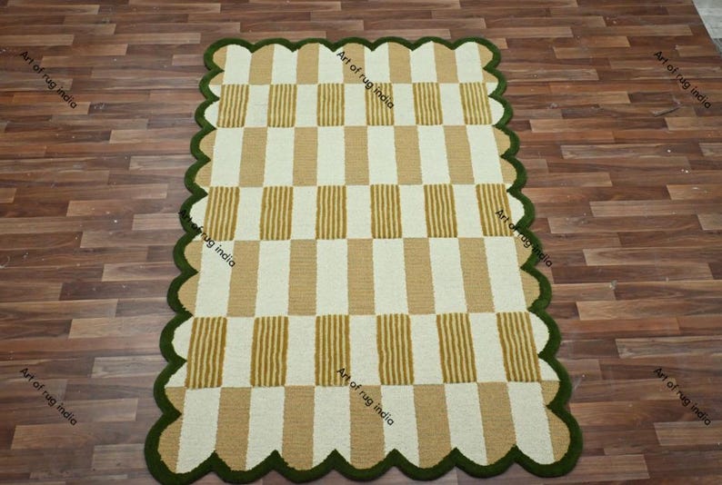 Puede incluir: Una alfombra rectangular con borde festoneado. La alfombra presenta un patr&oacute;n de rayas verticales alternas en beige y blanco. El borde es de color verde oscuro. La alfombra est&aacute; sobre un suelo de madera.