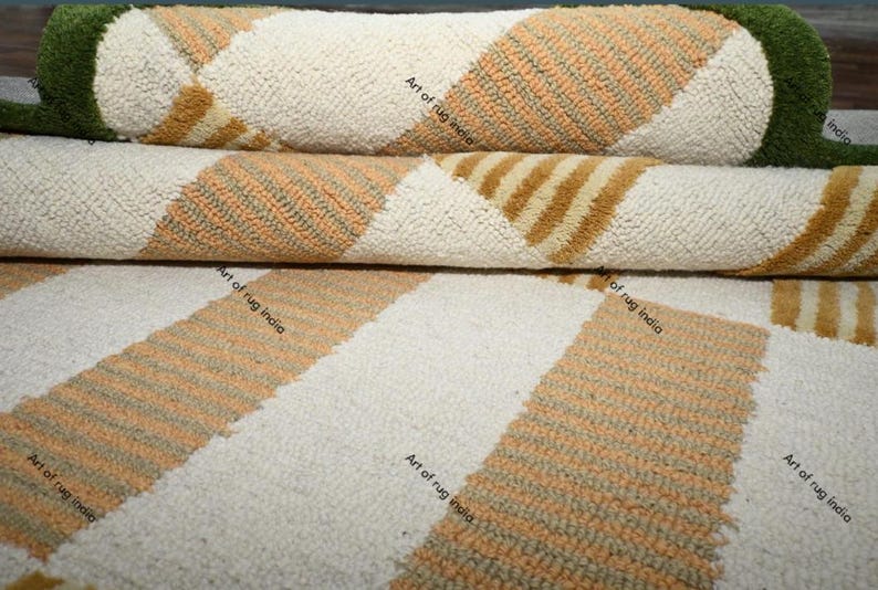 Puede incluir: Primer plano de alfombras enrolladas con un patr&oacute;n geom&eacute;trico. Las alfombras presentan un fondo crema con rayas diagonales en tonos naranja y marr&oacute;n. Los bordes de las alfombras son verdes.