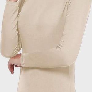 Pu&ograve; includere: Una maglia a collo alto beige a maniche lunghe. L'indumento ha una vestibilit&agrave; aderente e un collo alto. Le maniche arrivano ai polsi e il tessuto appare liscio. Lo stile generale &egrave; semplice e versatile, adatto per la stratificazione o da solo.