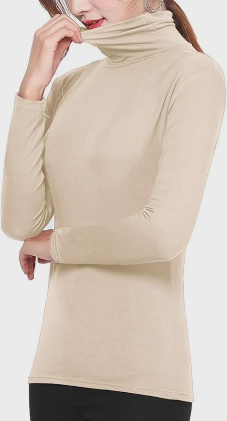 Pu&ograve; includere: Una maglia a collo alto beige a maniche lunghe. L'indumento ha una vestibilit&agrave; aderente e un collo alto. Le maniche arrivano ai polsi e il tessuto appare liscio. Lo stile generale &egrave; semplice e versatile, adatto per la stratificazione o da solo.