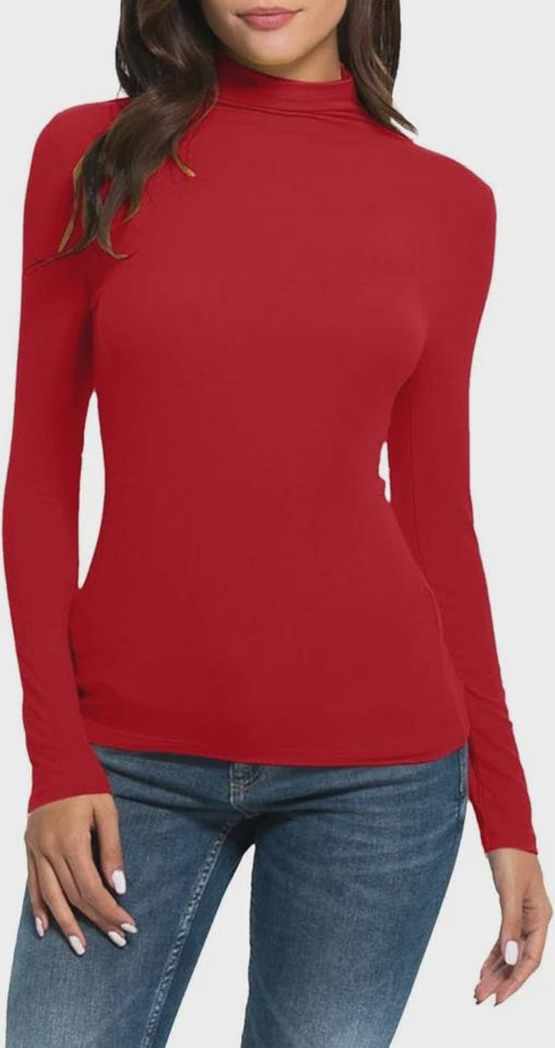 Pu&ograve; includere: Una maglietta rossa a maniche lunghe con collo alto. La maglietta &egrave; di colore unito e sembra essere fatta di un materiale morbido ed elastico. La modella indossa jeans blu.