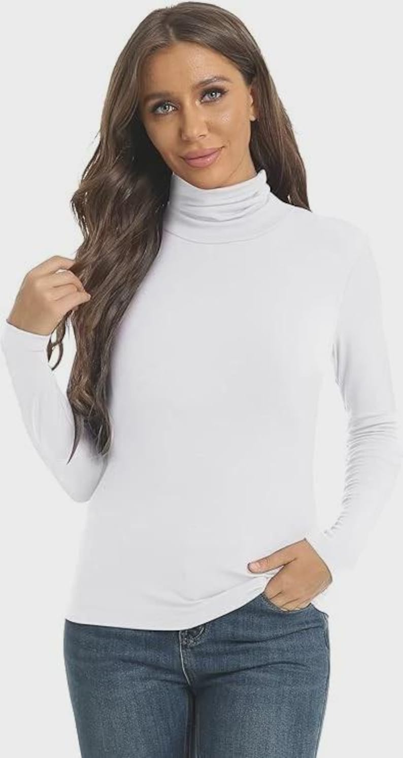 Pu&ograve; includere: Una maglietta bianca a maniche lunghe con collo alto. La maglietta &egrave; realizzata in un materiale morbido ed elastico ed &egrave; abbinata a jeans blu. La modella indossa la maglietta e i jeans.