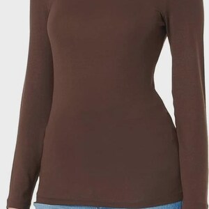 Pu&ograve; includere: Una maglia a maniche lunghe e collo alto marrone. La maglia &egrave; di colore uniforme e sembra essere realizzata in un materiale morbido e aderente. La modella indossa jeans blu.