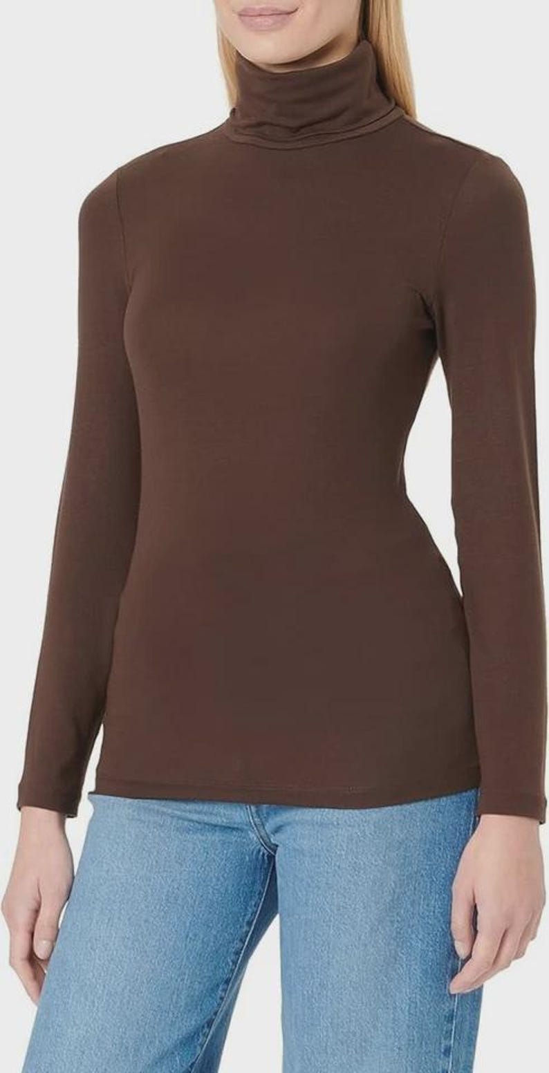 Pu&ograve; includere: Una maglia a maniche lunghe e collo alto marrone. La maglia &egrave; di colore uniforme e sembra essere realizzata in un materiale morbido e aderente. La modella indossa jeans blu.