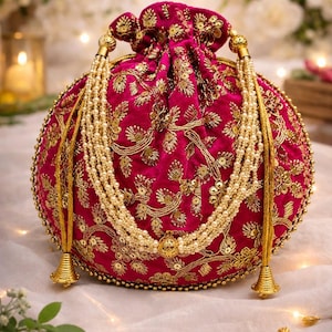 Peut inclure: Un sac bourse en velours fuchsia orné de broderies au fil d'or, de motifs floraux et de paillettes dorées. Le sac est agrémenté de plusieurs rangs de perles artificielles couleur crème et de pompons en métal doré à la base.