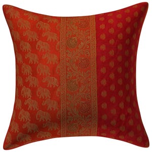 May include: Square cushion with a vibrant red and gold design. The cushion features three distinct sections: one with repeating elephant patterns, a central floral border, and a dotted pattern. The colour palette includes shades of red and gold.