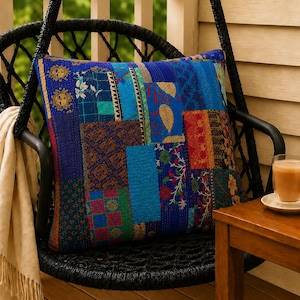 Könnte beinhalten: Ein quadratisches Zierkissen mit einem Patchwork-Design aus verschiedenen blauen, roten und grünen Stoffbahnen mit komplexen Blumen-, geometrischen und Sonnenmotiven. Das Kissen weist durchgehend sichtbare Steppnähte im Kantha-Stil auf.