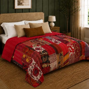 May include: A red patchwork quilt featuring a variety of floral and geometric patterns in shades of red, white, yellow, and black. The quilt is draped over a bed with white and tan pillows, showcasing intricate stitching across the fabric surface.