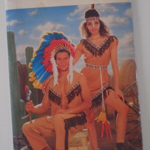 Peut inclure: Une enveloppe de patron Butterick vintage représentant deux personnes en costumes d'inspiration amérindienne. Les costumes sont de couleur beige avec des franges noires et des accents de plumes. L'homme porte une coiffe avec des plumes bleues, rouges et blanches.