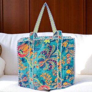 Handmade Indian floral velvet tote bag with blue base placed on a wooden table near window and plants.
