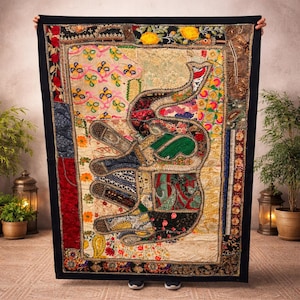 Puede incluir: Un gran tapiz rectangular con un borde negro. El tapiz presenta un colorido diseño de patchwork con un motivo de elefante. El elefante está compuesto por varias telas en tonos de rojo, verde, azul y dorado, con intrincados patrones y adornos.
