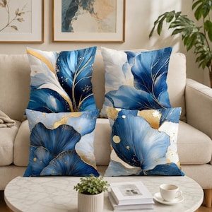May include: A set of four square scatter cushions featuring a fluid abstract pattern in shades of deep blue, white and gold. The design displays sweeping petal-like shapes with gold-coloured speckles and veins across the fabric surface.