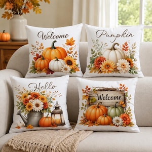 Peut inclure: Quatre coussins carrés en tissu blanc avec des motifs sur le thème de l'automne. Les designs incluent des citrouilles, des tournesols, des feuilles d'automne, un arrosoir en métal, une lanterne et un panneau en bois avec le texte Welcome, Pumpkin ou Hello.
