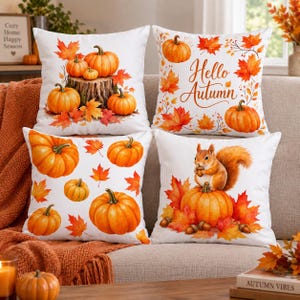 Könnte beinhalten: Ein Set aus vier quadratischen Dekokissen mit weißen Bezügen und herbstlichen Illustrationen. Die Motive zeigen orangefarbene Kürbisse auf einem Baumstumpf, den Schriftzug Hello Autumn mit Ahornblättern, verstreute Kürbisse und ein Eichhörnchen.