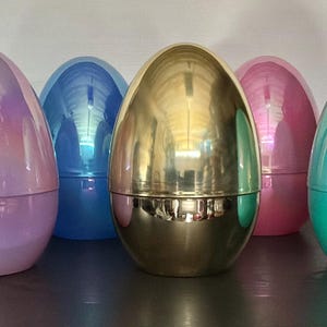 May include: A collection of iridescent Easter egg-shaped containers in various colors, including green, purple, blue, gold, pink, and teal. The containers are arranged in a row, reflecting light and creating a shimmering effect. These decorative eggs are ideal for Easter.