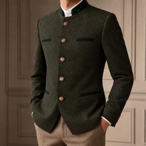 Puede incluir: Una chaqueta de mezcla de lana en color verde oliva oscuro con cuello mao, cinco botones metálicos en la parte delantera y dos bolsillos ribeteados horizontales en el pecho. La chaqueta se lleva sobre una camisa blanca y pantalones beige.