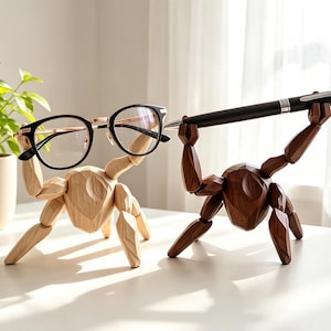 May include: Two faceted wooden figures in light and dark brown tones. The light figure holds black-rimmed glasses with rose gold accents, while the dark figure holds a black ballpoint pen with silver trim, both posed in a lifting position.