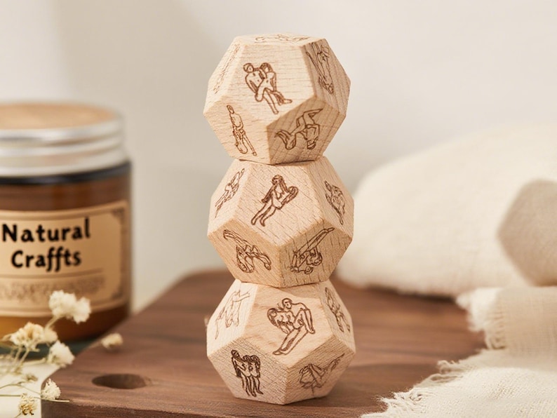 May include: Three wooden, dodecahedron-shaped blocks stacked on top of each other. Each block is engraved with various illustrations of human figures. The blocks are light brown and rest on a dark brown wooden surface.