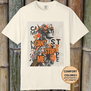 May include: Cream-coloured t-shirt with a graphic design that reads "CAN'T STOP ME". The design features a woman in sunglasses and a collage of colourful elements. The shirt is garment-dyed for a soft, vintage feel.