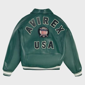 May include: Green leather jacket featuring the word "AVIREX" arched across the back, above a circular patch with the American flag and the text "ESTABLISHED 1975". The word "USA" is below the patch. The jacket has a white and green striped hem and cuffs.