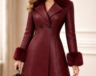 May include: A burgundy-colored coat with a faux fur collar and cuffs. The double-breasted coat has a tailored fit and a flared skirt. A black handbag is held in the hand.