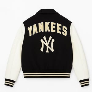 Op de afbeelding: Zwart-witte varsity jas met "Yankees" in gouden letters op de rug, samen met het logo van het team. De jas heeft witte mouwen, een zwarte body en gestreepte details op de manchetten en zoom. Een klassiek sportkledingstuk.