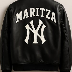 May include: Black leather jacket with the name "MARITZA" in white block letters above a white "NY" logo. The jacket has a black ribbed collar, cuffs, and hem. A stylish outerwear piece.