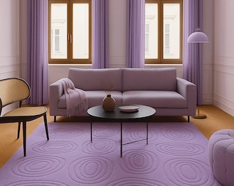 May include: A living room scene with a lilac color scheme. The room features a lilac rug with concentric circle patterns, a matching sofa, curtains, and a round coffee table. A paper lantern and floor lamp add to the decor.
