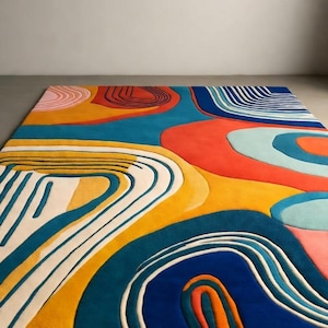 Op de afbeelding: Een rechthoekig vloerkleed met een abstract ontwerp. Het kleed heeft een kleurrijk ontwerp met gebogen lijnen en vormen in blauw, oranje, geel en roze. Het ligt op een grijze vloer en biedt een moderne, artistieke uitstraling. De afmetingen van het kleed zijn in centimeters.