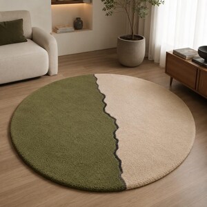Puede incluir: Una alfombra circular con un diseño de dos tonos, que presenta una sección de color verde oliva oscuro y otra de color beige claro. Ambos colores están separados por una línea oscura, ondulada e irregular que atraviesa verticalmente la superficie.