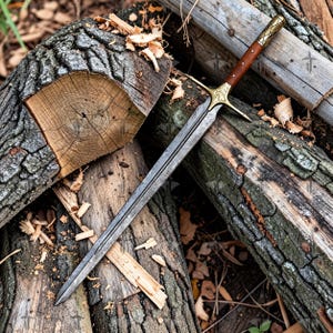 May include: A long sword with a dark, textured steel blade featuring a central fuller. The hilt consists of a brown wooden grip, a gold-colored crossguard with intricate floral engravings, and a matching gold-colored pommel with a crosshatch pattern.