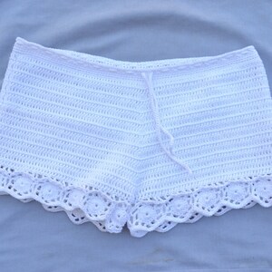 May include: White crochet shorts with a lace trim. The shorts have a drawstring waist.