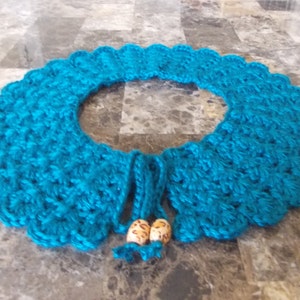 May include: Teal blue crocheted collar with two wooden beads attached to the ties.