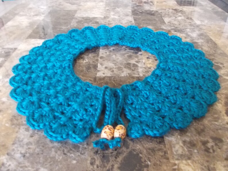 May include: Teal blue crocheted collar with two wooden beads attached to the ties.