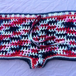 May include: Crocheted shorts in a colorful pattern of red, white, blue, and pink. The shorts have a drawstring tie at the waist.