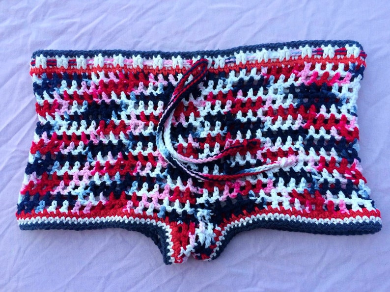 May include: Crocheted shorts in a colorful pattern of red, white, blue, and pink. The shorts have a drawstring tie at the waist.