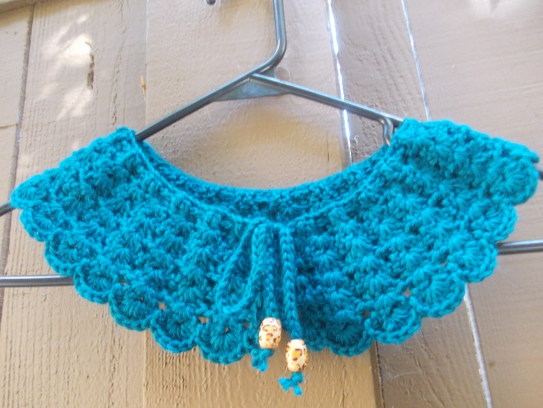 May include: A teal blue crocheted collar with a scalloped edge and a beaded tie.