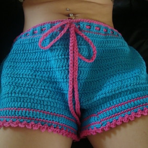 Könnte beinhalten: Blaue Häkelshorts mit einem rosa gehäkelten Bund und Besatz. Die Shorts haben einen Gürtel an der Taille.