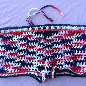 May include: Crocheted shorts in a red, white, and blue color pattern. The shorts have a tie at the top.