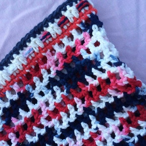 May include: Close-up of a crocheted fabric with a pattern of red, white, blue, and pink yarn. The fabric is made with a simple stitch and has a loose, airy feel.