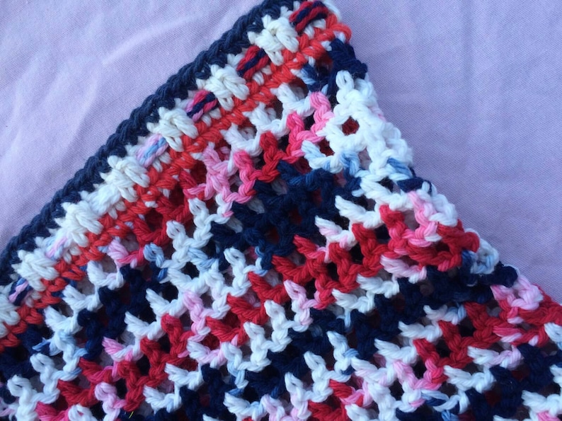 May include: Close-up of a crocheted fabric with a pattern of red, white, blue, and pink yarn. The fabric is made with a simple stitch and has a loose, airy feel.
