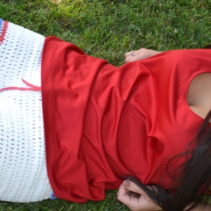 May include: A white crocheted shorts with red and blue trim, worn with a red sleeveless top. The person is lying on green grass.