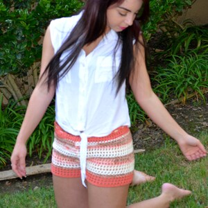 May include: A woman wearing a white button-down shirt with a crocheted skirt in shades of orange, white, and brown. The skirt has a high waist and a loose fit.