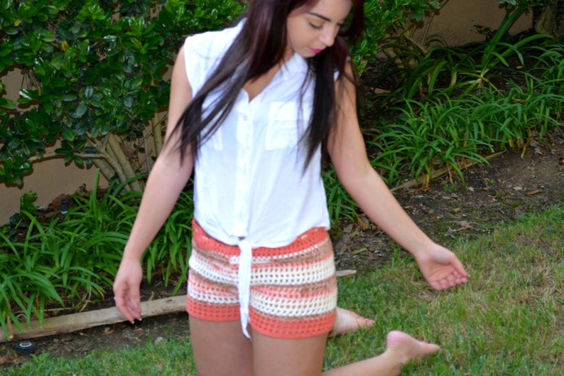 May include: A woman wearing a white button-down shirt with a crocheted skirt in shades of orange, white, and brown. The skirt has a high waist and a loose fit.