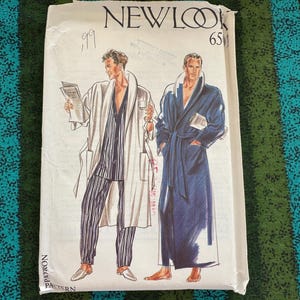 Op de afbeelding: Een vintage New Look 6511 naaipatroon met illustraties van twee figuren in badjassen. Eén figuur draagt een gestreepte pyjama en een witte badjas, de ander een blauwe badjas. Het patroon heeft een witte achtergrond.