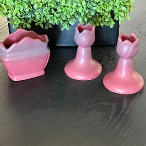 May include: Three vintage pink ceramic candle holders. Two are shaped like tulips and one is a small planter.