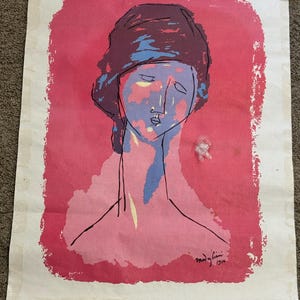 May include: A vintage art print featuring a stylized portrait of a woman. The artwork uses a limited color palette of pink, blue, and brown, with black outlines. The print is signed "Modigliani 1916".
