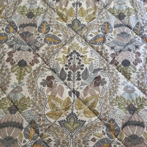 May include: A quilted fabric featuring a repeating botanical pattern in shades of sage green, mustard yellow, muted brown, and gray on an off-white background. The textile is stitched with a diamond grid pattern throughout the entire surface.