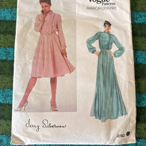 May include: Vintage Vogue Patterns American Designer sewing pattern. The pattern features illustrations of two long dresses. The pink dress has a fitted bodice and flared skirt. The teal dress has a high neck and long sleeves. The pattern is signed by Jerry Silverman.