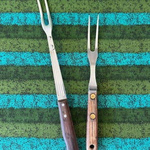 May include: Two vintage meat forks with wooden handles. One fork has a long, fluted metal handle and a dark brown wooden handle. The other fork has a shorter, light-colored wooden handle. Both forks have two tines.